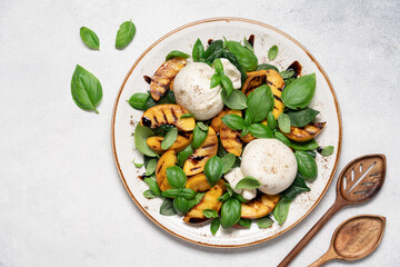 Mediterranean salad with burrata cheese, grilled peaches, fresh basil leaves, olive oil and balsamic glaze, gourmet summer dish on light background