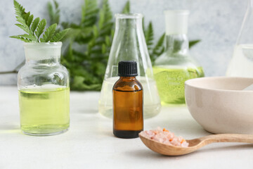 Bottle of oil, laboratory glassware with samples and ingredients for preparing natural cosmetics on white table near grunge wall