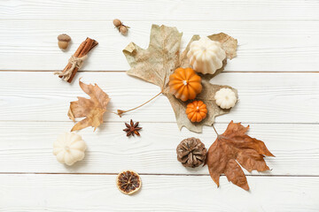 Autumn composition with candles in shape of pumpkins, fallen leaves and spices on light wooden background