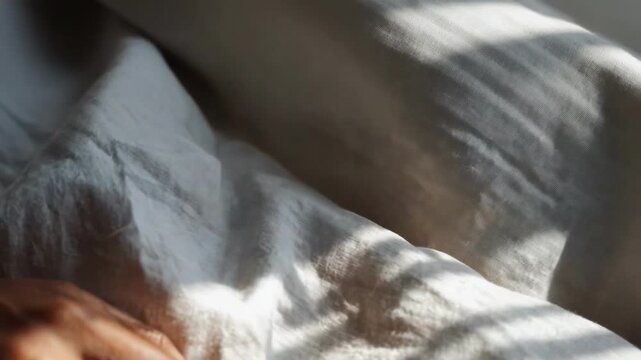 A hand resting on a white bedsheet with soft light illuminating the fabric.