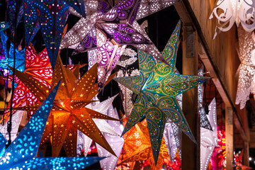 Naklejka premium Decorative star shaped lanterns in vibrant colors and patterns hang at a holiday craft stall at Christmas markets,