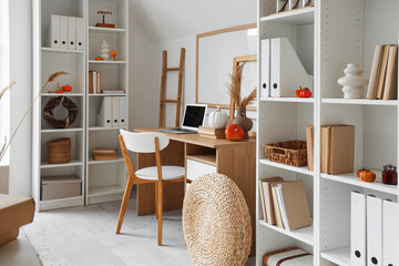 Interior of light living room with autumn decor, workplace and shelf units