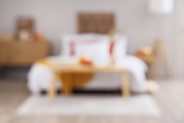 Interior of modern bedroom with soft bed, chest of drawers and pumpkins on coffee table, blurred...
