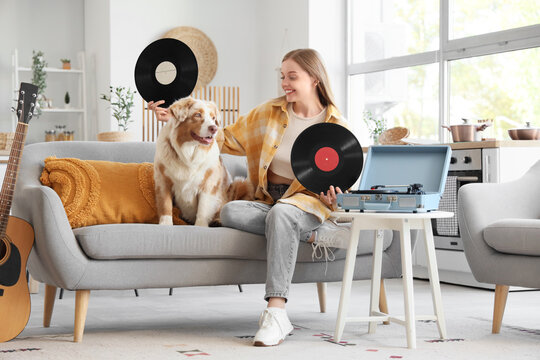 Young woman with vinyl disks for record player and Australian Shepherd dog sitting on sofa at home