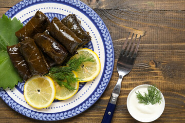Plate with tasty Dolmas (stuffed grape leaves), lemon slices and sour cream on wooden background