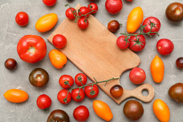 Wooden board with different fresh tomatoes on grey background