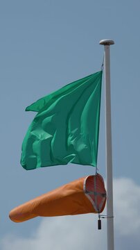 Green Safety Flag and Windsock Blowing on Sunny Beach