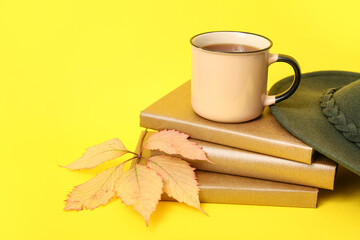 Books, cup of tea, stylish hat and autumn leaf on yellow background