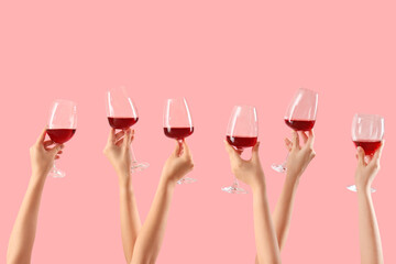 Female hands holding glasses of red wine on pink background