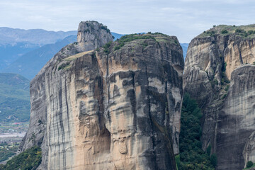 A towering rock formation rises from a forested valley in Meteora