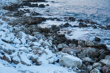 Winter seascape snow. The steep bank is strewn with snow. A small silhouette in the distance. The concept of winter holidays, walks along the sea, enjoyment and privacy. Evening subdued sunset light