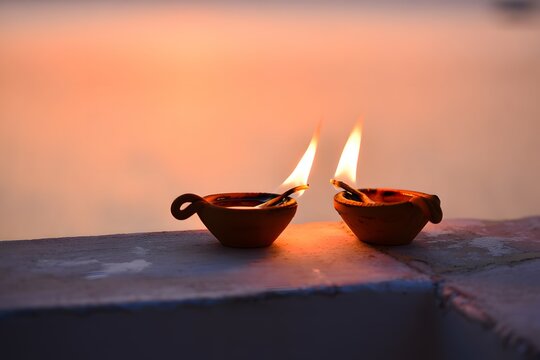 Two earthen diyas glowing during diwali festival with a warm orange background light