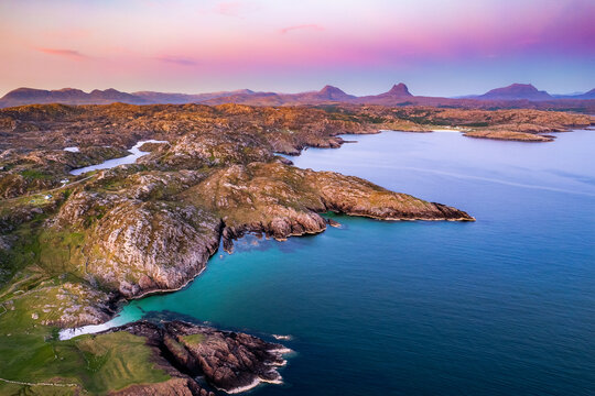 Aerial view of the rugged coastline meeting the turquoise sea under a pastel sky, Assynt, Lairg, Scotland, United Kingdom. - Powered by Adobe