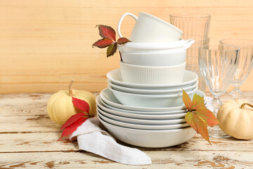 Stack of dishes with autumn decor and pumpkins on table against wooden background