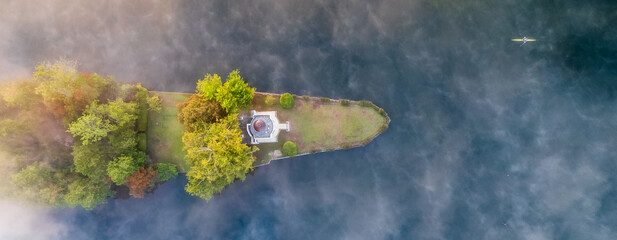 Aerial view of an island with a white temple shrouded in mist, where a lone kayaker glides across the tranquil waters, Henley-on-Thames, Oxfordshire, England, United Kingdom.