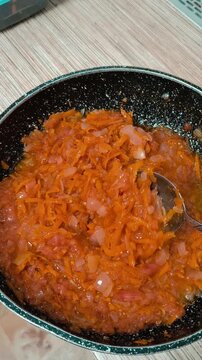 A person stirs stewed vegetables with a spoon. A hand with a spoon stirs food. Stewed vegetables. Sun-dried tomatoes. Tomato paste. Home cooking.