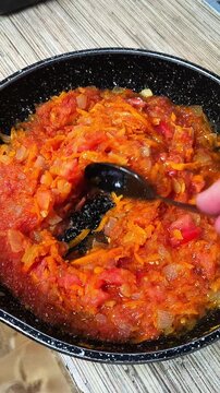 A person stirs stewed vegetables with a spoon. A hand with a spoon stirs food. Stewed vegetables. Sun-dried tomatoes. Tomato paste. Home cooking.