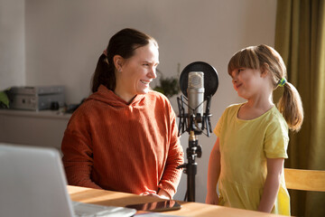 Smiling mother and little daughter in front of microphone talking and recording podcast in home creating content for online blog. blogging concept.