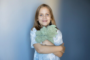 Child smiling while holding green stuffed animals in a cozy indoor setting during the day