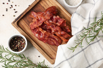 Wooden board with fried bacon rashers, rosemary and bowl of peppercorn on white background