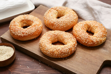 Cutting board of tasty bagels with sesame seeds on wooden background, closeup
