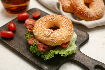 Wooden board of tasty bagel sandwich with fried bacon and tomatoes on white background