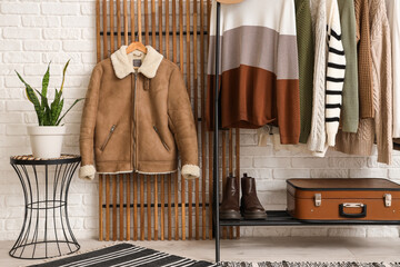 Rack with stylish sweaters near white brick wall in room