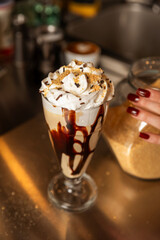 Preparation of a milkshake made with crushed biscuits, milk, whipped cream, and chocolate syrup in a glass