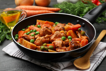 Delicious cooked stew in frying pan and ingredients on black table, closeup