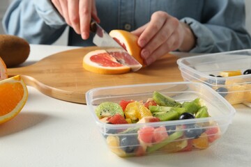 Making fruit salad. Woman cutting grapefruit at white table, closeup