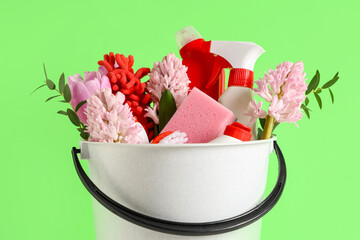 Cleaning supplies with spring flowers on green background, closeup