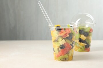 Tasty fruit salad in plastic cups on beige table, closeup. Space for text
