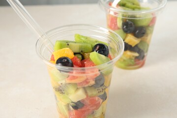 Tasty fruit salad in plastic cups on beige table, closeup