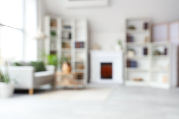 Fototapeta premium Shelves with books, sofa and fireplace in interior of modern living room. Blurred view