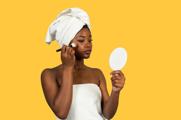 Black woman applying makeup looking in hand mirror