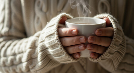Close-up of hands holding a warm cup of tea or coffee while wearing a cozy sweater