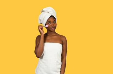 Black woman wrapped in towel applying skincare mask