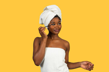 Young black woman applying makeup on yellow background