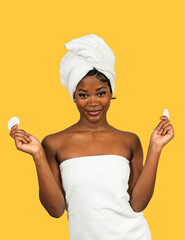 Young black woman holding cotton pads performing skincare routine