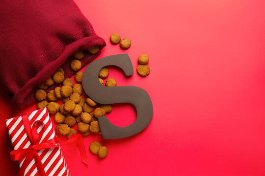 Saint Nicholas (Sinterklaas) day. Chocolate letter S, kruidnoten cookies and gift box on red background, flat lay. Space for text