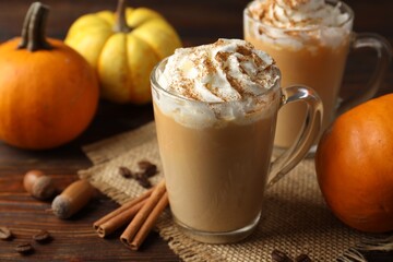 Tasty pumpkin latte with whipped cream in glass cups and ingredients on wooden table, closeup