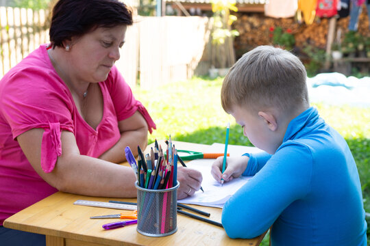 Grandmother and grandson drawing together outdoors, fostering creativity and bonding in a sunny backyard setting.