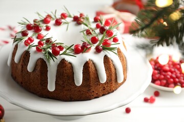 Tasty Christmas cake with icing, cranberries and rosemary on white table, closeup