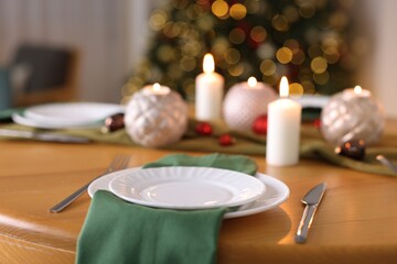 Stylish Christmas table setting with plates, cutlery and burning candles in festive decorated room, closeup. Bokeh effect