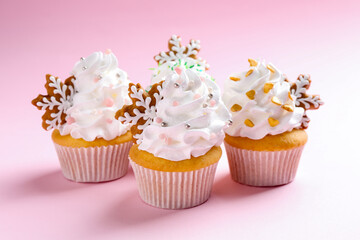 Tasty cupcakes with Christmas decor on pale pink background, closeup