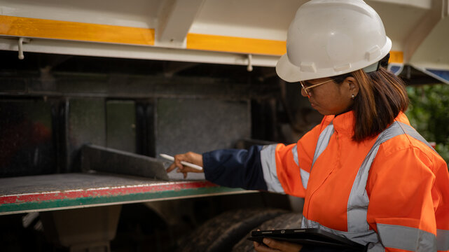A worker in a safety vest and hard hat examines a truck at a construction site. The sun casts a warm light, highlighting safety equipment and focused work - Powered by Adobe