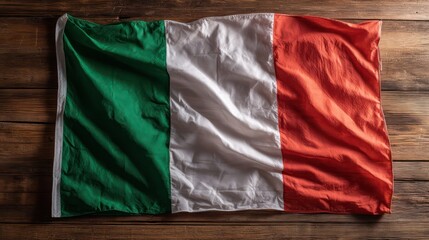 Italy flag lying flat on smooth wooden surface, natural grain beneath translucent fabric. Controlled studio lighting enhances texture