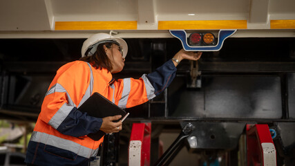 A worker in safety gear checks the equipment beneath a truck in a construction zone. The scene...