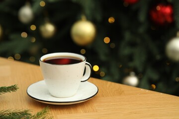 Aromatic coffee in cup and fir tree branches on wooden table against blurred lights, closeup. Space for text