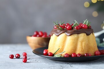 Delicious Christmas cake with chocolate glaze, cranberries and rosemary on grey textured table against blurred lights, closeup with space for text. Bokeh effect